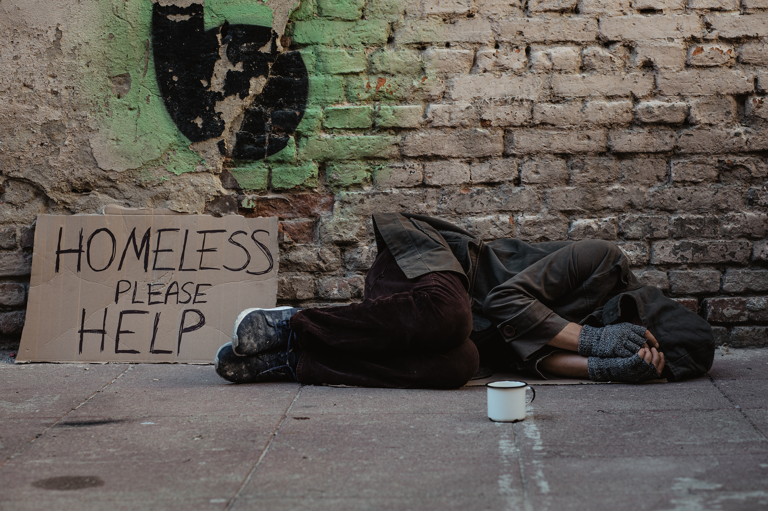 Photo of homeless man lies on the street in the shadow of the old building