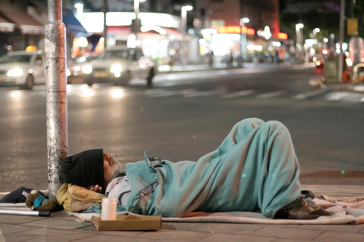 Photo of homeless man sleeping on busy city street. Photo by Adobe Stock