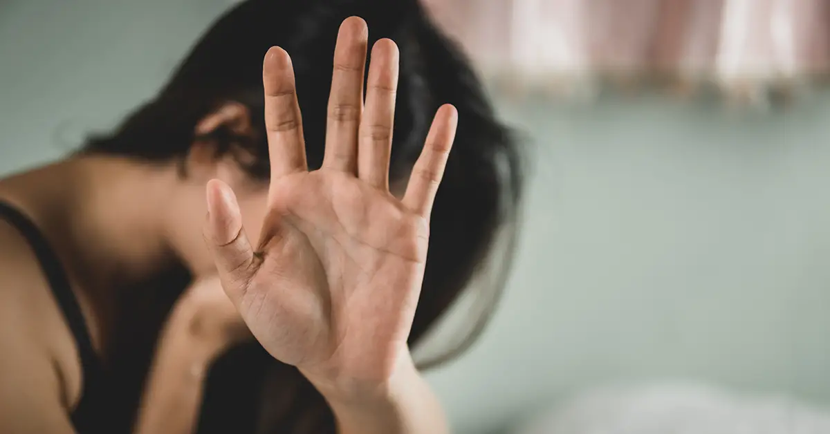 Photo of a woman crying while raising one hand to the camera to block her face from being seen. Photo by AdobeStock.