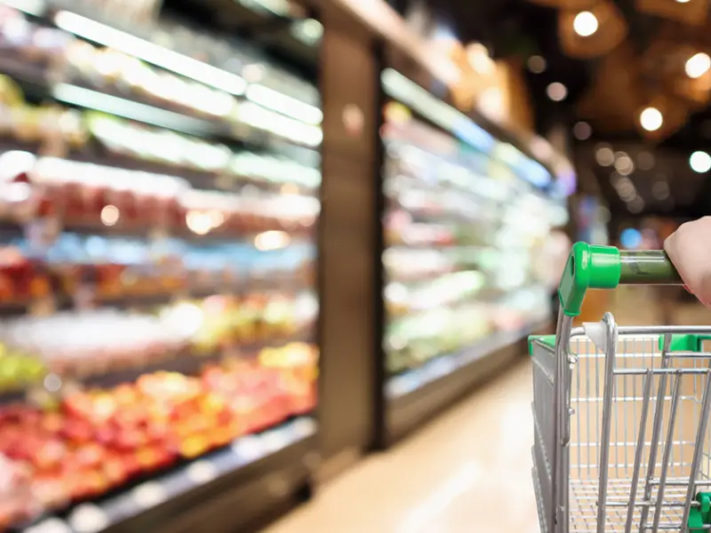 Close up image of a person pushing a shopping cart through a grocery store. Photo by Adobe Stock.