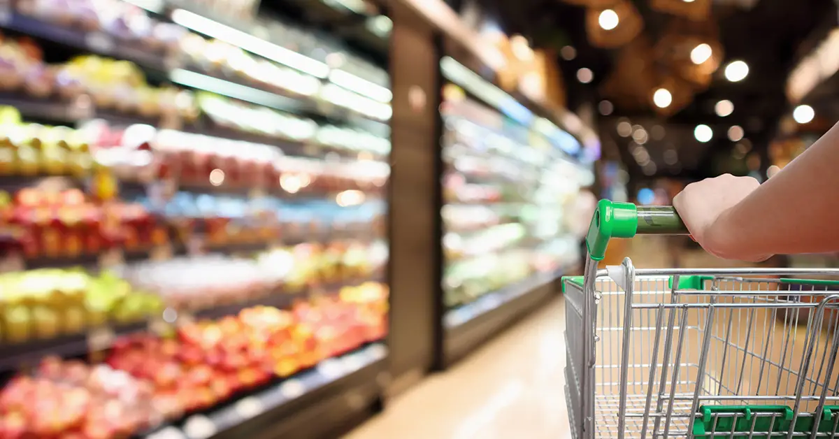 Close up image of a person pushing a shopping cart through a grocery store. Photo by Adobe Stock.