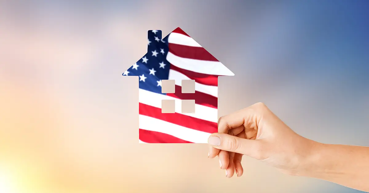 Photo of a person's hand holding a logo of a house that is colored with the image of the U.S. flag.