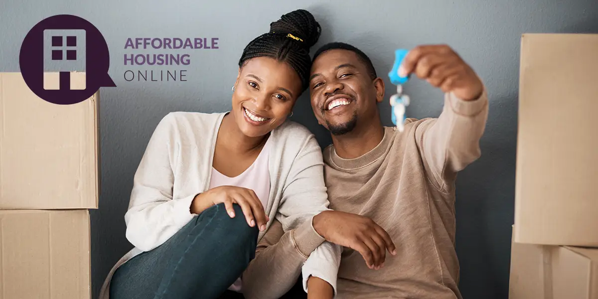 Photo of a man and a woman sitting close together with arms intertwined, as the man holds up a set of keys to their new home. Affordable Housing Online logo is placed in the corner.