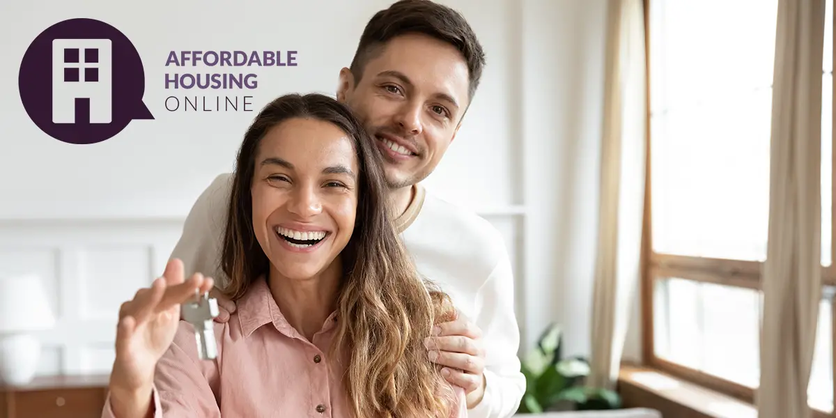 Photo of a husband and wife smiling at the camera while inside their new apartment, as the wife holds up a set of keys, with the Affordable Housing Online logo.