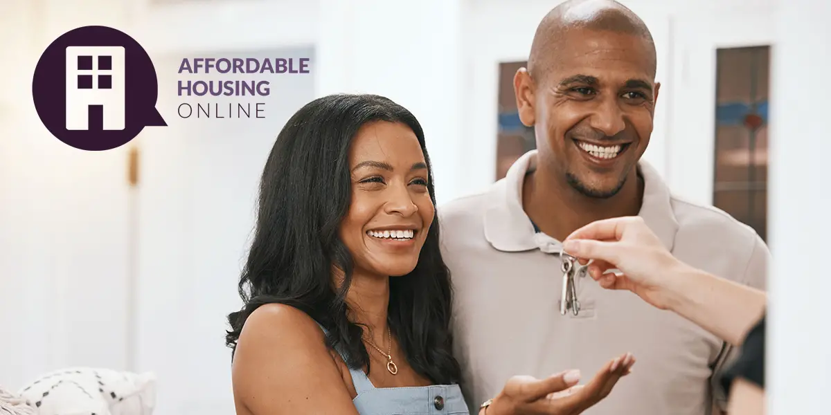 Photo of a man and woman smiling, as the woman reaches out with her hand to be given keys to their new home.