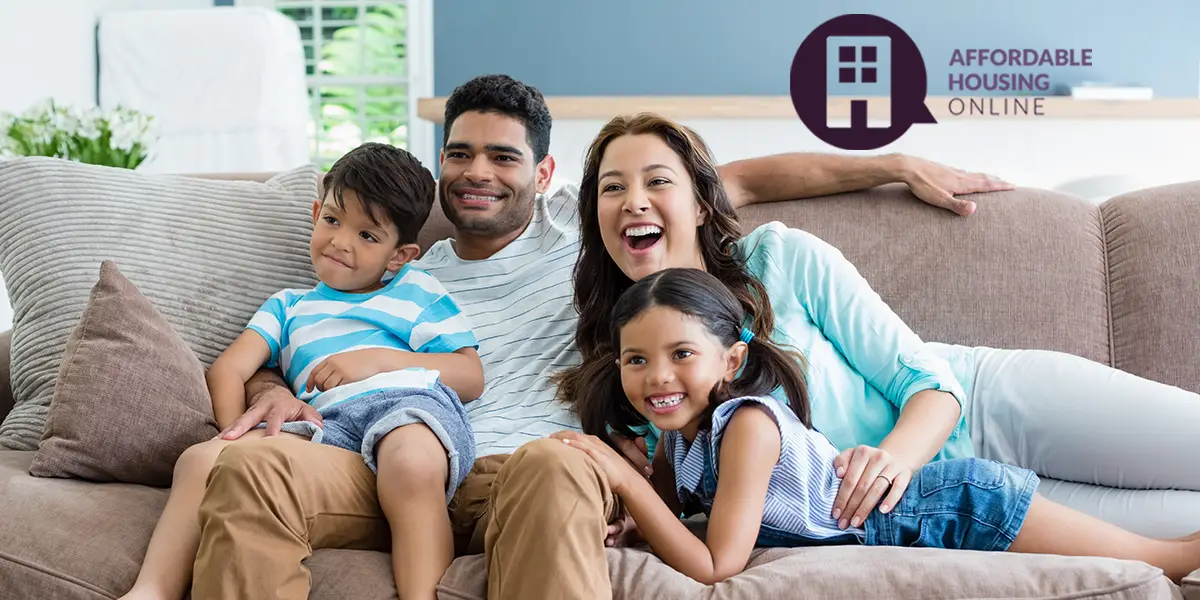 Photo of a family of four sitting on the couch of their new home. The father, mother, son, and daughter are all smiling and looking to the right.